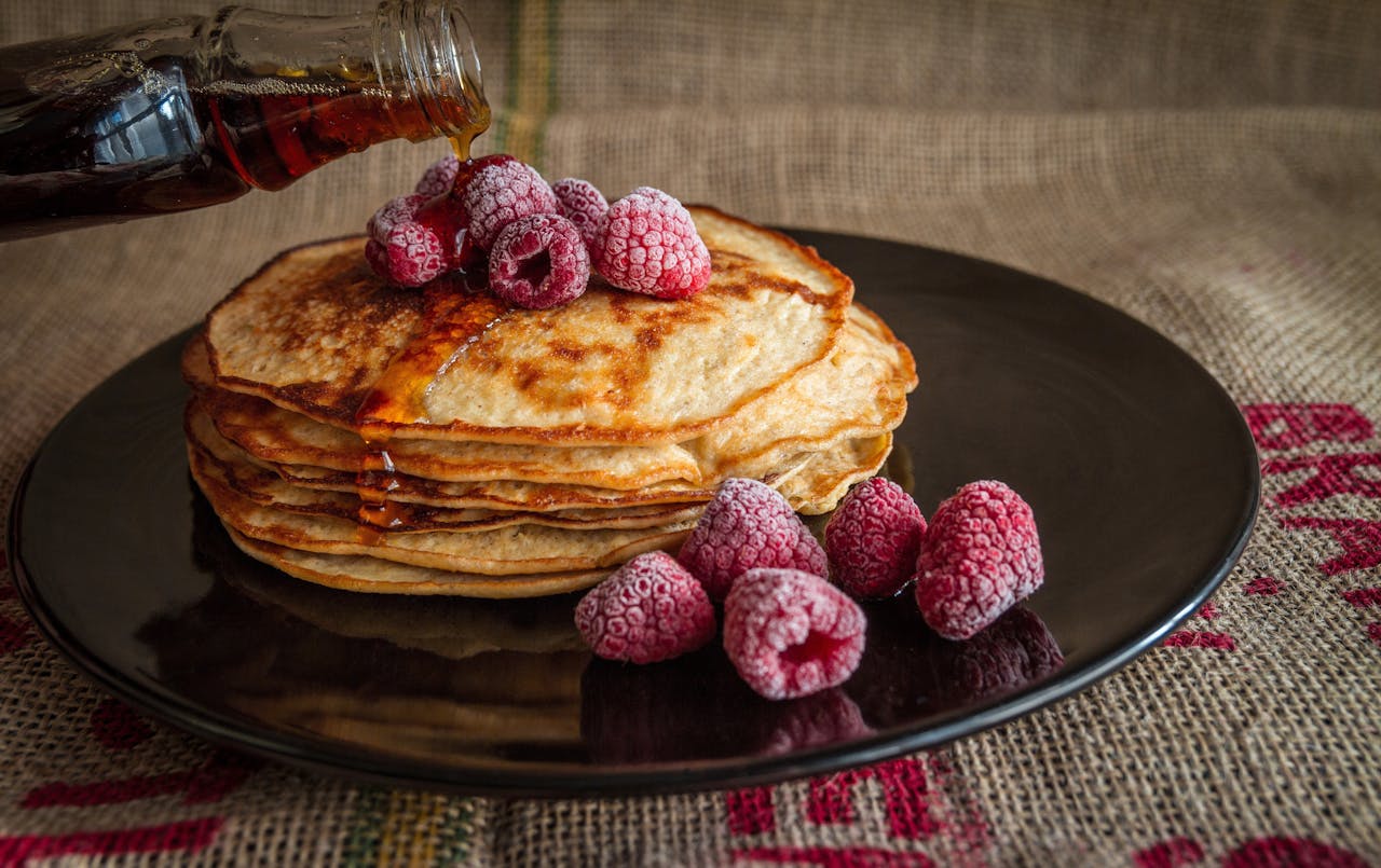 journey Stack of pancakes topped with raspberries and syrup on a dark plate.