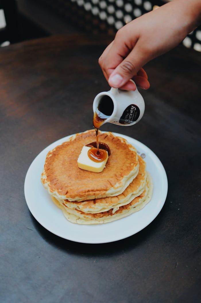 services-02 Delicious stack of pancakes topped with butter and maple syrup being poured.