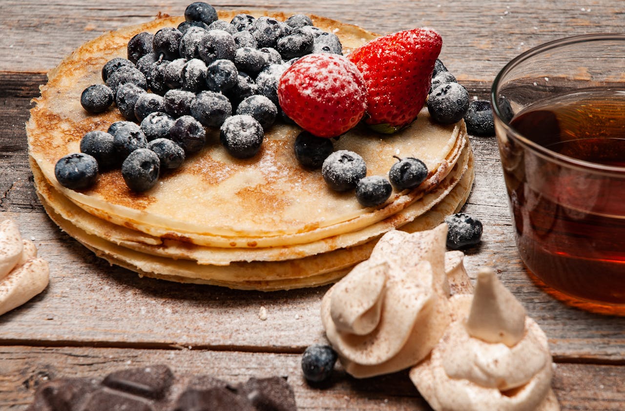 services-03 Stack of homemade pancakes topped with fresh blueberries and strawberries, served with syrup.