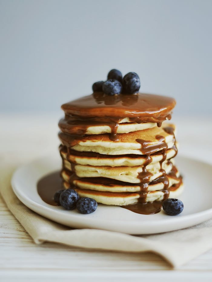 services-04 Mouth-watering pancakes stacked with blueberries and syrup on a plate.