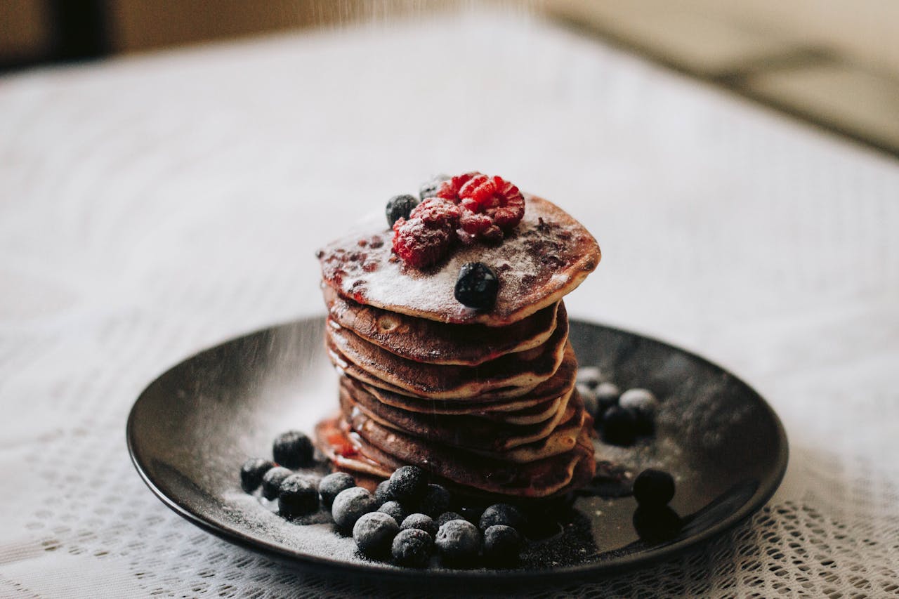 Stack of fluffy pancakes adorned with fresh blueberries and raspberries, dusted with sugar.